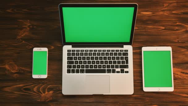 Top view shot of three elecronic devices with green screen on a wooden background. White smartphone, tablet device and laptop compyter. Chroma key — Stock Video