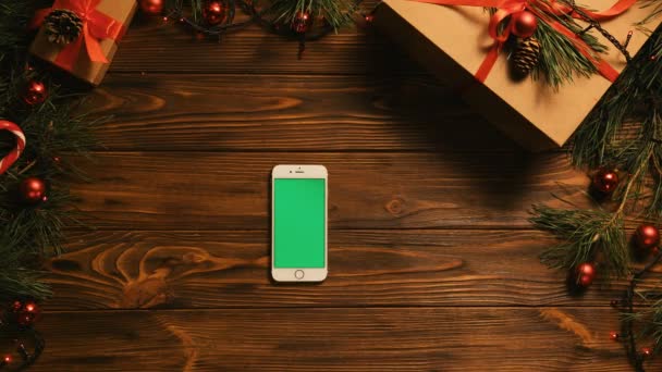 Conceito de Natal. Vista superior. Smartphone branco com tela verde na velha mesa de madeira com decoração de Natal. Chave Chroma — Vídeo de Stock