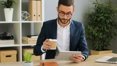 Ofiste kahve yudumlarken ve onun tablet cihaz office özgeçmişlerine bakarak meşgul genç adam. Kapalı atış.