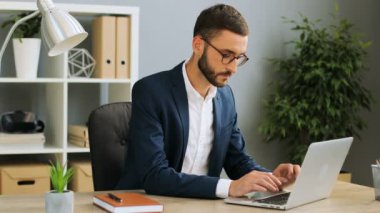 Modern ofis dizüstü bilgisayarda yazarak emin iş adamı. Beyaz erkek dizüstü bilgisayarınızın ekranına masanın üzerinde arıyorsunuz, o zaman defter ve düzenlemeler yapmak için kalem alarak.