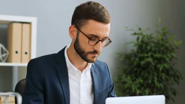 Young busy businessman in a suit working at the trendy office. Caucasian male looking into the screen of the laptop on the desk. — Stock Video