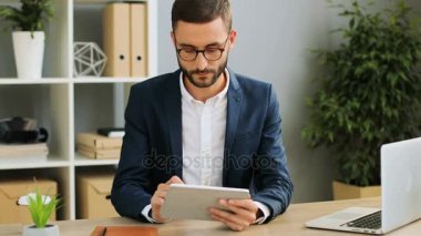 Genç attracive iş adamı tablet kullanma ve çok modern ofisinde çalışıyor. Kapalı atış.