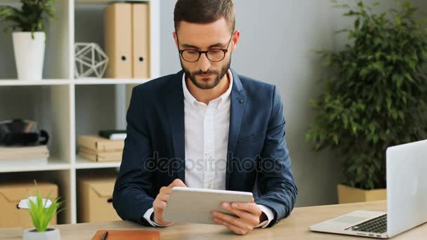 Atrakcją młody biznesmen przy użyciu tabletu i ciężko pracuje w nowoczesnym biurze. Wewnątrz strzał. — Wideo stockowe