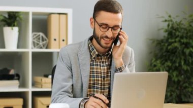 Mutlu bir adam ofis masa başında oturan, telefonda konuşurken ve bir meslektaşı ile görüşme sırasında memnun ve tatmin hissi bardaklarda görüntüsünü kapatın. Kapalı atış.