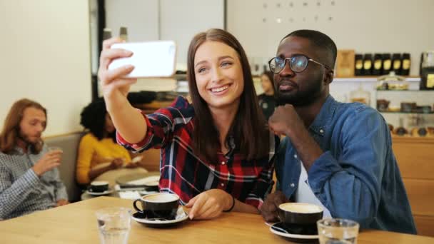 Amigos felizes fazendo caras engraçadas ao tirar selfie no smartphone no fundo da cafeteria. Interior . — Vídeo de Stock