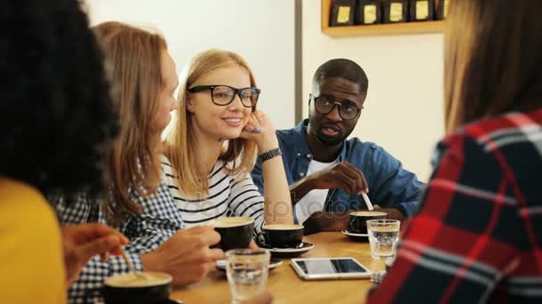 Foto lateral de un grupo de mujeres multiétnicas y un hombre charlando y divirtiéndose juntos en un acogedor café de la ciudad en un día. De cerca. . — Vídeos de Stock