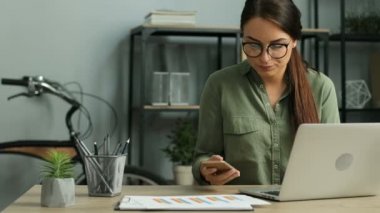 Modern ofis dizüstü bilgisayarla çalışırken kağıt belgeleri tutan kızgın iş kadın cep telefonundan savunarak. Yakın çekim