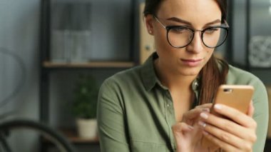 Modern kentsel ofiste çalışırken smartphone kullanarak bardaklarda çekici kadın. Tarama, dokunmatik ekran dokunarak ve gülümseyen kadın. Yakın çekim