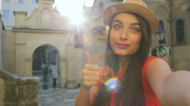 Kamera ve smilimg açık havada güzel eski sokakta, başparmak gösterilmesini genç mutlu traveler kadın. Yakın çekim