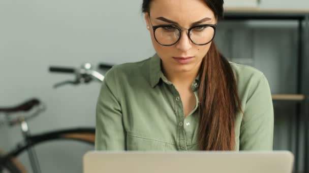 Primer plano de la joven atractiva mujer con gafas y el trabajo con el ordenador portátil en la oficina urbana moderna. Mujer pensando mientras mira la ventana . — Vídeo de stock