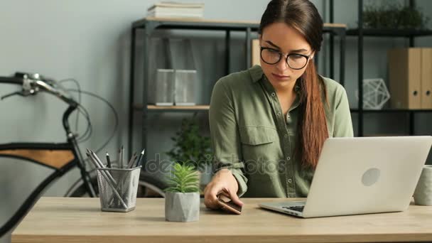 Atractiva mujer de negocios morena hablando en el teléfono celular mientras trabaja con computadora portátil en la oficina urbana moderna. La mujer tiene conversación. De cerca. — Vídeos de Stock