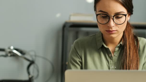 Primer plano de la joven atractiva morena con gafas de trabajo con ordenador portátil en la oficina urbana moderna. Mujer escribiendo en el teclado, la lectura, el surf inernet . — Vídeos de Stock