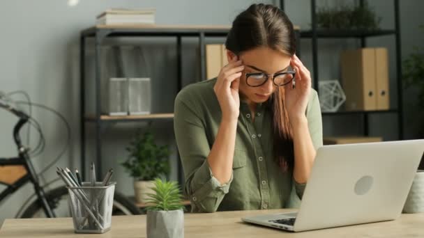 Joven empresaria cansada quitándose las gafas mientras trabaja en el portátil en la oficina, sintiendo dolor de cabeza y masajeando las sienes. De cerca. — Vídeos de Stock