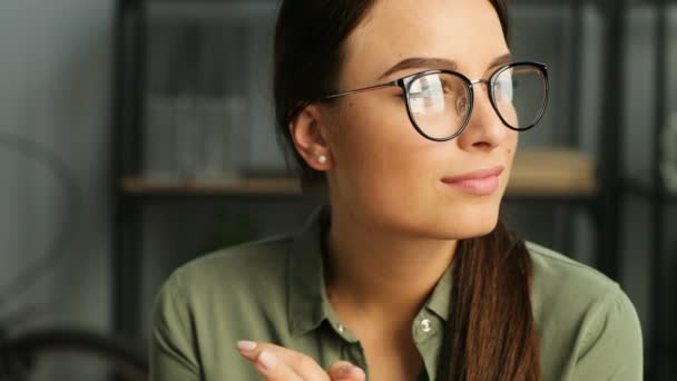 Retrato de una mujer de negocios hermosa y exitosa en gafas mirando a la ventana y a la cámara y sonriendo. De cerca. Mujer trabajando en la oficina — Vídeos de Stock