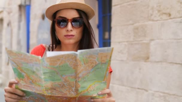 Молода красива жінка в сонцезахисних окулярах дивиться деякі туристичні пам'ятки на паперовій карті і шукає правильну вулицю, місце. Жінка, яка подорожує в старому місті. крупним планом — стокове відео