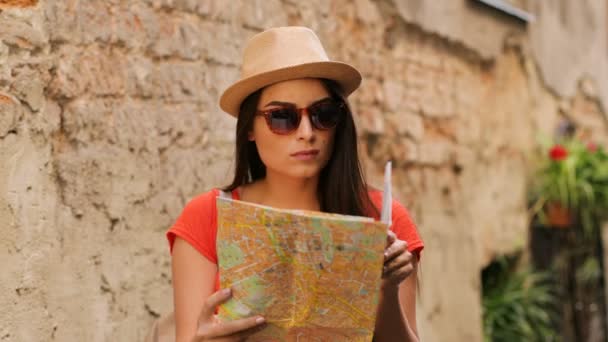 Mujer atractiva joven en gafas de sol mirando en el mapa de papel para las atracciones turísticas. Mujer de turismo en el casco antiguo. De cerca. — Vídeo de stock