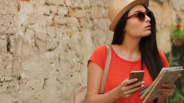 Mujer atractiva joven turismo en la ciudad vieja. Viajero femenino utilizando el mapa en papel y mapas en línea en el teléfono inteligente para encontrar lugares interesantes. De cerca. — Vídeos de Stock