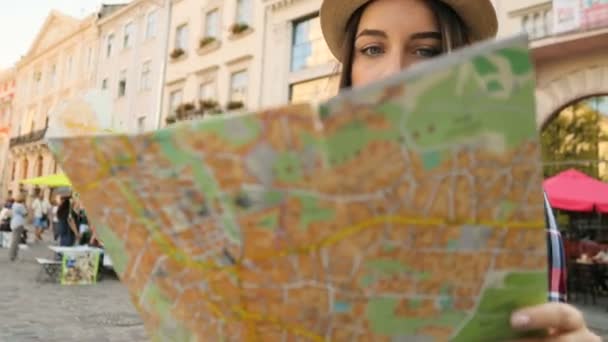 Молодая женщина в шляпе ищет на туристической карте нужную улицу. Девушка ищет улицу с картой. Женщина путешествует. close up — стоковое видео
