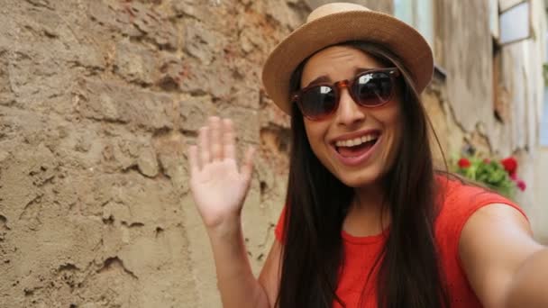 Νέων ελκυστικών τουριστικών γυναίκα έχοντας συνομιλία μέσω βίντεο σε εξωτερικούς χώρους σε δρόμο της παλιά πόλης. Γυναίκα κουνώντας και χαμογελά στη φωτογραφική μηχανή. κοντινό πλάνο — Αρχείο Βίντεο