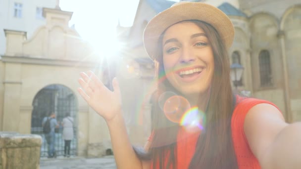 Schöne fröhliche junge Frau Video-Chat während der Reise in der Altstadt mit schönen Architektur Gebäuden. Frau winkt in die Kamera. Nahaufnahme. — Stockvideo