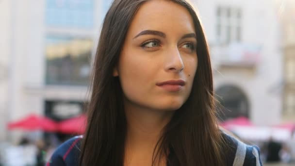 Retrato de la cara de una joven atractiva girando la cabeza a la cámara y sonriendo alegremente en la calle de la ciudad. De cerca. . — Vídeo de stock