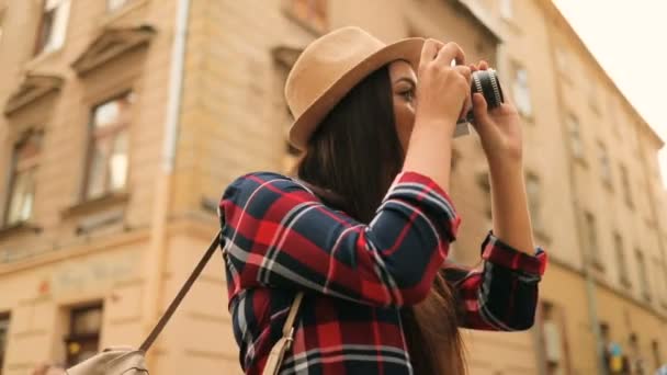 Hermosa joven con un sombrero elegante tomando fotos de los edificios antiguos en la cámara vintage de pie en la calle de la ciudad. Ronda dolly tiro — Vídeo de stock