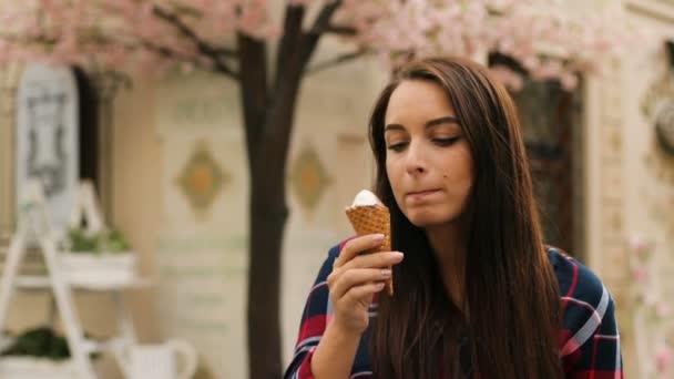 Joven morena comiendo sabroso helado al aire libre en la calle de la ciudad y mirando a la cámara . — Vídeo de stock