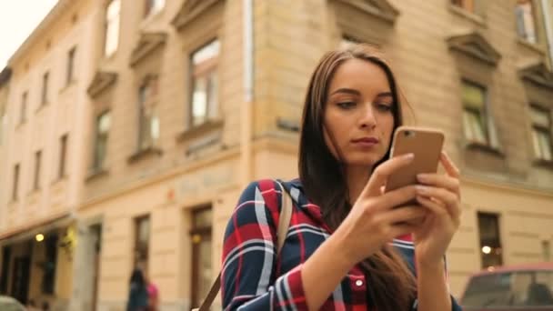 Jonge brunette vrouw met behulp van smartphone terwijl staande in het midden van de straat. Vrouw het texting, surfen op het internet. Ronde dolly schot — Stockvideo