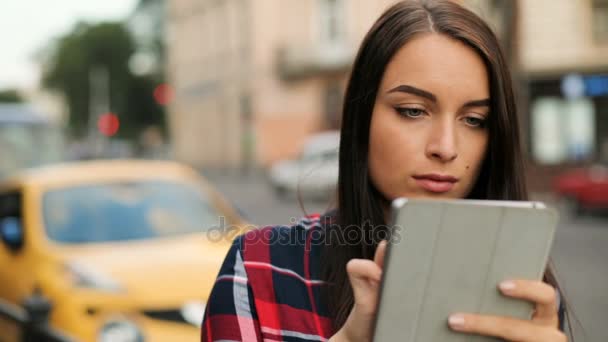Fiatal nő az utcán sétálva tabletta eszköz segítségével. A nő megérinti a touchscreen, és körülnézett. Közelről. Elmosódott háttér — Stock videók