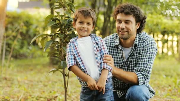 Close-up. Portret van een kleine jongen en zijn papa planten van een boom. Ze lachen en kijken naar de camera. Onscherpe achtergrond — Stockvideo