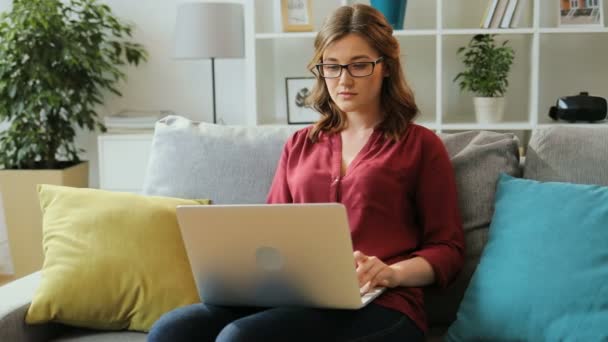 Ung allvarlig kvinna i glasögon använder laptop för att arbeta i hem i vardagsrummet. — Stockvideo