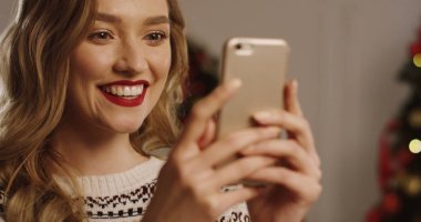 Genç gülümsedi ve kayıt ve cep telefonu sohbet ve sürpriz yüzüm mutlu sarışın kadın yakın çekim. Noel ağacı arka planda. Portre vurdu.