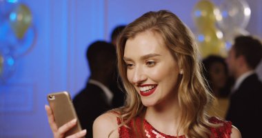 Akıllı telefonunu kayıt ve neşeyle gülerek lüks partide genç sevimli kadın. İnsanlar ve balon arka plan üzerinde dans ediyor. Kapalı