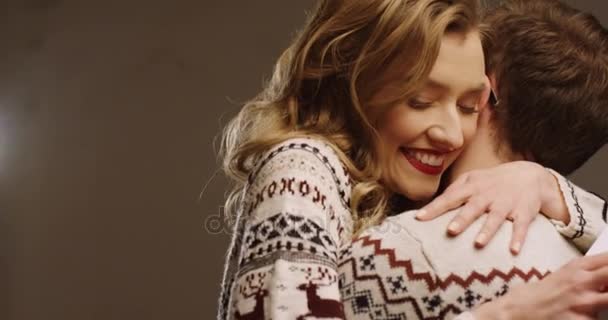 Gros plan d'une jeune femme blonde heureuse tenant son cadeau de Noël et embrassant son mari dans la chambre décorée pour Noël. À l'intérieur. Portrait — Video