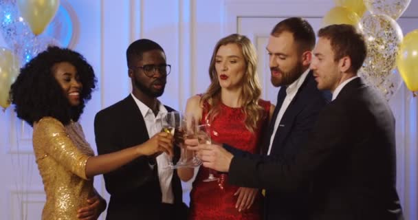 Junge multiethnische Menschen, die Champagner trinken und bei der glamourösen Party mit Gläsern jubeln. Freunde, die etwas feiern. drinnen — Stockvideo