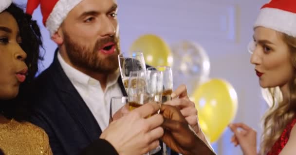 Primer plano de amigos multiétnicos en los sombreros de Santa Claus haciendo vítores con gafas de Champaigne en la fiesta de Año Nuevo. Celebrando el tiempo. En el interior. Retrato — Vídeos de Stock