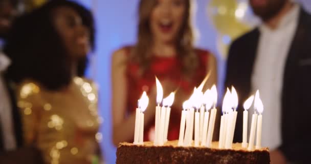 Close-up do bolo de aniversário com velas está sendo levado e a mulher de aniversário entre seus amigos está no fundo borrado. Festa de aniversário. Interior — Vídeo de Stock