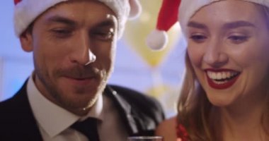 Genç insanlarda gülümsüyor: santa claus şapka ve gözlük dökme şampanya kapatın. Yeni yıl arifesinde parti. İçeride. Portre vurdu