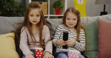 TV izlerken, modern oturma odasında popcorns ile kanepede otururken gülüyor iki sevimli küçük kız. İçinde