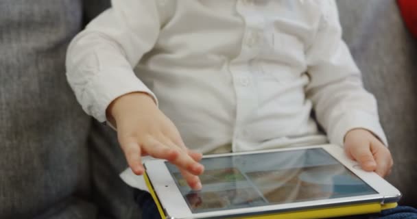 Nahaufnahme des Tablet-Computers, der auf den Beinen der Kinder liegt, und der Kinderhand, die ihn hält und darauf spielt. zu Hause. innen — Stockvideo