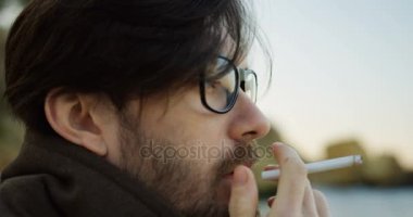 Çekici melankolik adamın gözlük bir sigara ve sahilde düşünme sakallı yakın çekim. Dışarıda. Portre