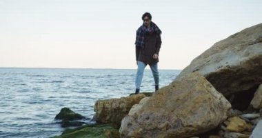 Sahil kayalarda yürürken çekici bir beyaz adam. Bulutlu gökyüzü ve soğuk hava. Dışarıda