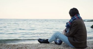 Yuvarlak bir kadeh sahil oturma ve bulutlu bir günde denize bakarak beyaz hoş adam. Arkadan