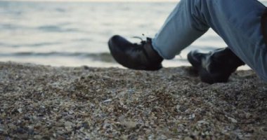 Denize oturan ve bir kum dökülen adam kadar kapatın. Bulutlu hava gün. Arkadan. Açık