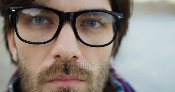 Close up van een scherpzinnige mannelijke blik. Kaukasische man in glazen en geruite sjaal. Onscherpe achtergrond. Buitenshuis. — Stockvideo