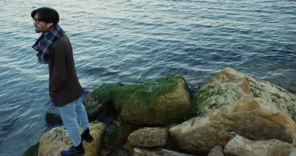 Uomo attraente in piedi sulle rocce costiere e guardando di fronte al mare. Tempo freddo. All'aperto. Vista dall'alto — Video Stock