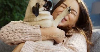 Sevimli genç kadının onun pug sarılma ve odaya evde otururken gülüyor pembe kazaklı kapatın. Portre. İçinde