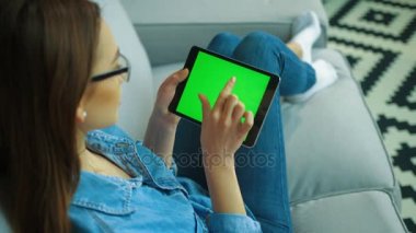 Oturma odasında kanepede otururken ile yeşil ekran siyah tablet bilgisayar kullanan güzel genç kadın. Kaydırma, sayfaları swiping eller kadın. Chroma anahtar. Üstten Görünüm