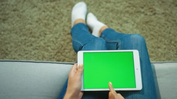 Mujer que usa tableta blanca con pantalla verde mientras está sentada en el sofá. Hembra manos páginas de desplazamiento, tocando en la pantalla táctil. Clave de croma. Vista superior. De cerca. — Vídeos de Stock