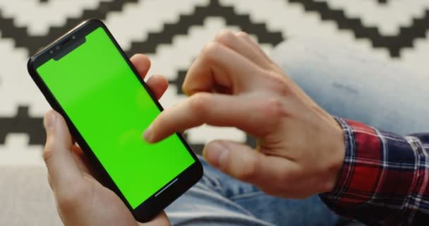 Feche as mãos dos homens segurando o smartphone preto verticalmente e rolando nele. Padrão borrado tapete de fundo. Vista superior. Tela verde. Chave Chroma . — Vídeo de Stock